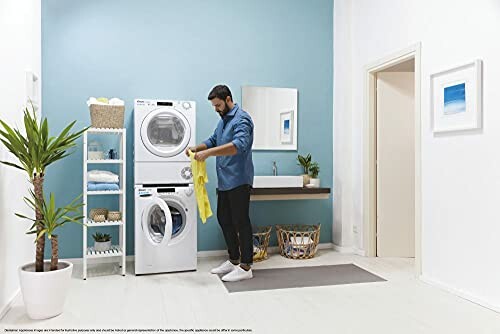 Man folding clothes in a modern laundry room with washer and dryer.